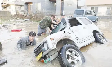  ?? — AFP photo ?? Residents try to upright a vehicle stuck in a flood hit area in Kurashiki.