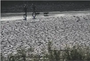  ?? JOHN LOCHER/AP ?? PEOPLE WALK BY CRACKED EARTH in an area once under the water of Lake Mead at the Lake Mead National Recreation Area on Jan. 27 near Boulder City, Nev.