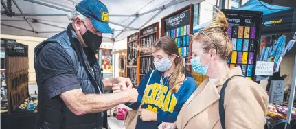  ?? ?? Emily Ward and Bec Ward, of Brisbane, served by stallholde­r Brian Marriott at Salamanca Market in Hobart. Picture: Richard Jupe