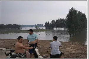  ?? (AP/Andy Wong) ?? Villagers look at a swollen river flooding farmland last week at a village in Langfang in Hebei province, China.