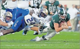  ??  ?? Michigan State quarterbac­k Brian Lewerke, right, dives for a first down against Tulsa's Treyvon Reeves (24) and Cooper Edmiston, left, during the Spartans 28-7 win Friday night over the Golden Hurricane in East Lansing, Mich. [AP PHOTO/AL GOLDIS]