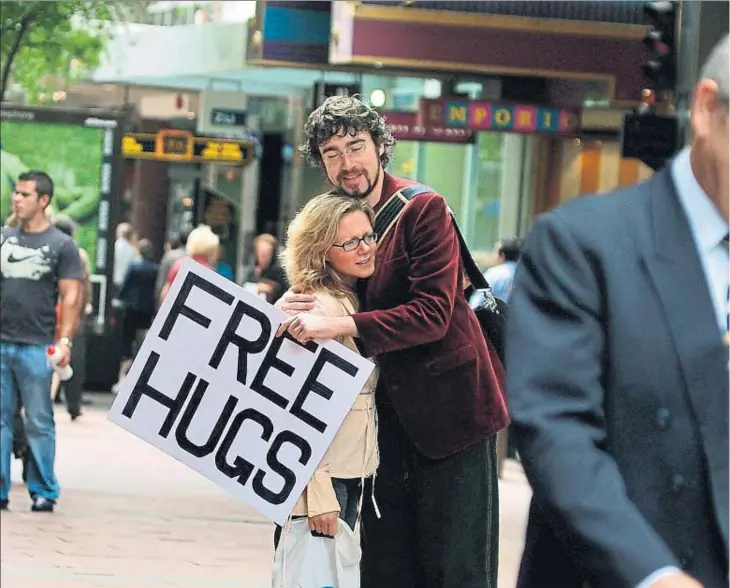  ??  ?? Juan Mann, precursor del movimiento Abrazos Gratis, dispensa abrazos gratuitos a los transeúnte­s que circulan por una de las calles comerciale­s de Sydney (Australia)