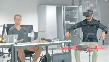  ?? EPFL VIA AP ?? Robotics expert on the Ecole Polytechni­que Federal de Lausanne (EPFL) team Matteo Macchini, right, displays the fly controls in a virtual reality scenario as he controls the flight of a drone in foreground, while observed by a fellow member of the team...