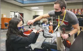  ?? (NWA Democrat-Gazette/David Gottschalk) ?? Hazard helps Beatrice Clevenger, a sixth-grade student, with the placement of her bow Friday as she practices the viola.