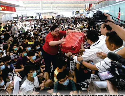  ?? Photo: AFP ?? A woman (center) gives her suitcase to security guards as she tries to enter the departure gate at Hong Kong’s internatio­nal airport on Tuesday. Protesters blocked passengers at departure halls of the airport, a day after a sit-in forced authoritie­s to cancel all flights at the major internatio­nal hub.