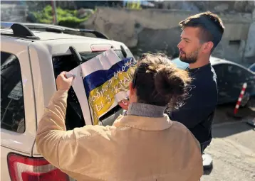  ?? (Maria Belkina/Reuters) ?? MARIA BELKINA and her partner, Kirill Zhivoi, co-founders of Volunteers Tbilisi, a group that helps refugees from Ukraine, stick a sign with the Ukrainian flag onto a vehicle in Tbilisi, Georgia, last month.