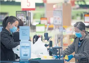  ?? JONATHAN HAYWARD THE CANADIAN PRESS FILE PHOTO ?? A grocery store worker wears a protective face mask and gloves as she watches a customer try to pay through the plexiglass divider. Premier Doug Ford has called such workers “heroes.”