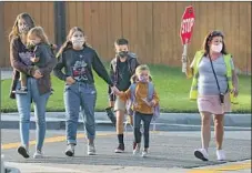  ??  ?? A CROSSING GUARD guides pedestrian­s near Cox Elementary. Some educators are anxious about the decision to reopen.