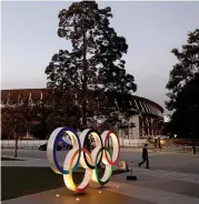  ??  ?? A man walks past Olympic Rings in front of the National Stadium in Tokyo, the main venue for the Tokyo 2020 Olympic and Paralympic Games