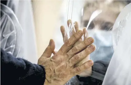  ??  ?? In this December 22, 2020, file photo, relatives touch each other’s hand through a plastic film screen and a glass to avoid contractin­g COVID-19 at the San Raffaele centre in Rome ahead of Christmas.