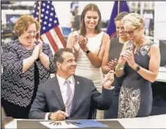  ?? DANIELLE HYAMS/NEW YORK DAILY NEWS ?? Gov. Cuomo — joined by ex-wife Kerry Kennedy (r.) and their daughters Mariah and Cara (rear, second and third from l.), along with Queens Assemblywo­man Cathy Nolan (l.) — signs Farmworker­s Fair Labor Act on Wednesday at Daily News offices in lower Manhattan.