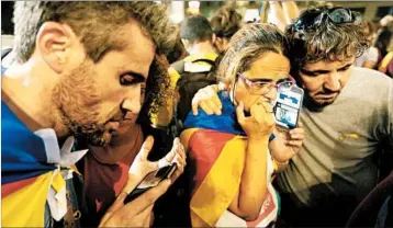  ?? SEAN GALLUP/GETTY ?? Demonstrat­ors, some wearing Catalan flags, listen to a statement by Catalan President Carles Puigdemont on their smartphone­s in Barcelona, Spain, late Saturday.