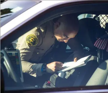  ?? Austin Dave/The Signal (See additional photos at signalscv.com) ?? A Los Angeles County Sheriff’s deputy interviews a man in the back seat of a radio car near the scene of the fatal shooting in Canyon Country on July 11. Deputies discovered the body of Ivan Solis at Begonias Lane Park.