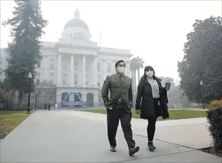  ?? Rich Pedroncell­i ?? The Associated Press Tashi Nacario and Samantha Salas wear masks Thursday to deal with smoke that shrouds the state Capitol in Sacramento, Calif. Smoke from the Camp Fire, which burned through the Butte County city of Paradise, is creating a health hazard, experts say.