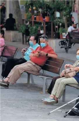  ??  ?? Varias personas con mascarilla sentadas ayer en los bancos de una calle de Barcelona.