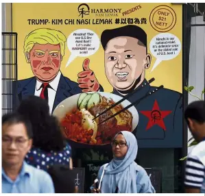  ?? — AP ?? Nuclear fusion cuisine: People walking past an advertisem­ent for ‘ TrumpKim Chi Nasi Lemak’ in Singapore.