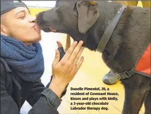  ??  ?? Danelle Pimentel, 20, a resident of Covenant House, kisses and plays with Molly, a 3-year-old chocolate Labrador therapy dog.