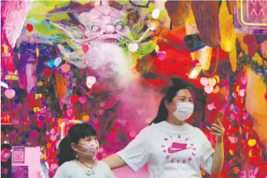 ?? ASSOCIATED PRESS PHOTO/NG HAN GUAN ?? Residents wearing masks visit a store decorated with a dragon sculpture Wednesday in Shanghai.