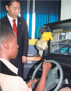  ??  ?? A student at Oracabessa High School in St Mary tests the virtual reality driving simulator donated by the Chinese Ambassador to Jamaica, Niu Qingbao (standing).