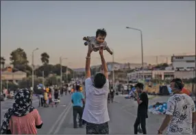  ?? (AP/Petros Giannakour­is) ?? A migrant holds up a baby as others gather Sunday on a road near Mytilene on the Greek island of Lesbos the same day Greek Prime Minister Kyriakos Mitsotakis demanded that the European Union take a greater responsibi­lity for managing migration.