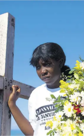  ?? (Photo: AP) ?? A woman holding flowers standing next to a cross honouring the victims of the 2010 earthquake before a memorial service at Titanyen, a mass burial site north of Port-au-prince, Haiti, on Saturday.