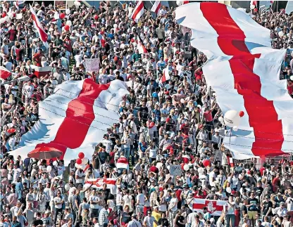  ??  ?? Protesters unveil the red and white flag of the Belarusian opposition; left, President Lukashenko addresses a pro-government rally, with supporters bussed in for the occasion