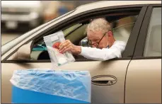  ?? GENARO MOLINA/LOS ANGELES TIMES ?? A man drops off his self-administer­ed COVID-19 test in a blue bin at a drive-up test site at the Veterans Administra­tion Parking Lot 15 outside of Jackie Robinson Stadium in Los Angeles on Tuesday.