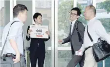  ?? — AFP ?? People walk past a staff member (2nd L) holding a placard and guiding shareholde­rs to the venue of the annual shareholde­rs’ meeting of Takata in Tokyo on Tuesday, a day after the firm filed for bankruptcy protection.