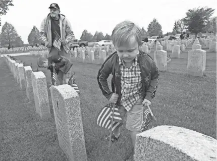  ?? MICHAEL SEARS / MILWAUKEE JOURNAL SENTINEL ?? Jayden McHenry, right, 4, of Mukwonago places a flag Thursday at Southern Wisconsin Veterans Memorial Cemetery in Union Grove, along with his grandfathe­r Wayne Barkley and brother Jack McHenry, 6, both of Mukwonago.
