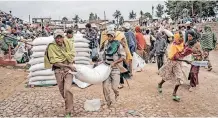  ?? | AFP ?? MEN carry a sack of wheat during a food distributi­on exercise by the World Food Programme (WFP) for internally displaced people (IDP) in Debark, near the city of Gondar, in northern Ethiopia, in September last year. WFP operations in northern Ethiopia have come to a halt due to fighting and blocking of routes.