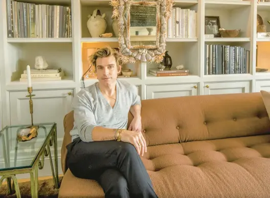  ?? TONY CENICOLA/THE NEW YORK TIMES PHOTOS ?? Interior designer Jeremiah Brent sits March 4 in front of the shelves he styled in the New York home he shares with his husband, Nate Berkus.