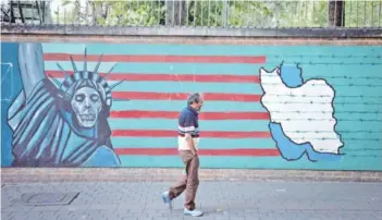  ??  ?? ► Un hombre camina por delante de un mural contra Estados Unidos en Teherán.