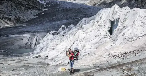  ?? FABRICE COFFRINI/AFP/GETTY IMAGES ?? A hiker takes a photograph as he stands next to a part of the Rhone Glacier, covered with insulating foam to prevent it from melting, near Gletsch, Switzerlan­d, on Friday.