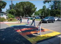  ?? LEZLIE STERLING THE SACRAMENTO BEE ?? Parents and students cross the street at a rainbow-colored crosswalk across from Birch Lane Elementary School in Davis. This is a perfect example of what it means when a speed limit sign says “When children are present.”