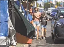  ?? Photograph­s by Francine Orr Los Angeles Times ?? MICHELLE BARON, left, walks with her daughter, Penelope, past a homeless encampment after school at Hollywood’s Larchmont Charter last month.