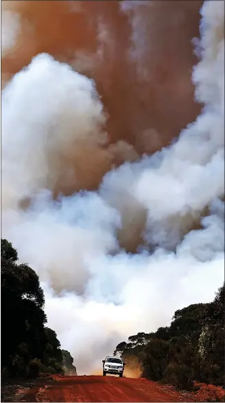  ?? Picture: LISA MAREE WILLIAMS/GETTY ?? EXIT: Smoke rises above Karatta as a vehicle speeds away yesterday