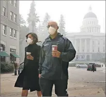  ?? Rich Pedroncell­i Associated Press ?? MATTELIN BAUTISTA and Stephen Penner wear masks Friday in Sacramento as Camp fire smoke shrouds the Capitol building.