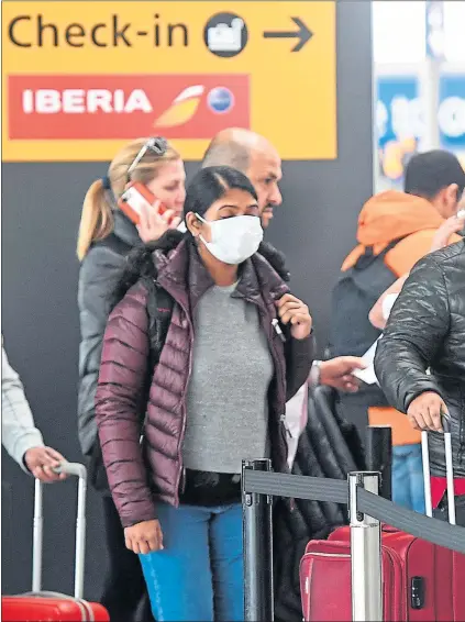  ??  ?? Travellers in masks queue at Heathrow airport in London as air travel grinds to a halt and nations across the world lock down their borders due to the coronaviru­s pandemic