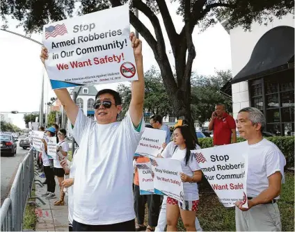  ?? Yi-Chin Lee / Houston Chronicle ?? Zhang Lu Zheng, left, hoists a poster during a Saturday protest against rising crime in the Chinatown neighborho­od and businesses. The protesters gathered at Westheimer and Post Oak to vent their concerns.