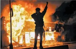  ?? JOHN MINCHILLO/AP ?? A demonstrat­or stands beside a building on fire Saturday in St. Paul, Minnesota.