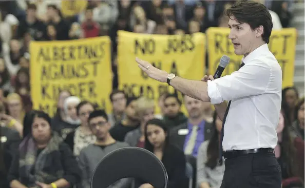  ??  ?? ED KAISER Pipeline protesters hold up signs Thursday night as Prime Minister Justin Trudeau speaks during his town hall at MacEwan University.