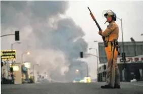  ?? ASSOCIATED PRESS FILE PHOTO ?? A California Highway Patrol officer stands guard at Ninth Street and Vermont Avenue in Los Angeles as smoke rises from a fire further down the street on April 30, 1992. It was the second day of unrest in Los Angeles following the acquittal of four Los...