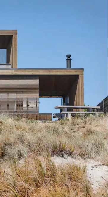 ??  ?? EXTERIOR Rising out of the dunes, the house affords a view from the sand to and through the front entrance on the left, while on the right (where there’s a concrete table and benches from Design Warehouse), you can see through the dining room and lanai to the grassed courtyard and garage beyond them. The sliding panels at the front of the home are made of cedar, which is also the prominent material chosen for the exterior cladding. Nicola says it performs very well, staying true, working with a stain and weathering nicely.