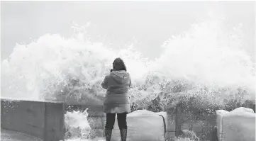  ??  ?? A woman takes photos of waves crashing against a tidal wall in Asnelles, northweste­rn France, after Storm Eleanor swept into Europe. — AFP photo