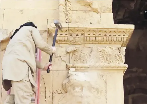  ?? The Associat ed Press ?? A militant hammers away at a face on a wall in Hatra, Iraq. Hatra is a large fortified city recognized as a UNESCO World Heritage site. ISIL is now a growing player in the US$3 billion global antiquitie­s market.