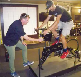  ?? J.P. SQUIRE/The Okanagan Weekend ?? Marty Tymm, manager of Fresh Air Concept in Kelowna, demonstrat­es the use of the Retul Body Geometry dynamic fit bike with sales associate and athlete Dalton Fayad.The machine measures the correct height of the saddle and its fore-and-aft position as well as the reach and angle of the human body as hands rest on the handle bars.