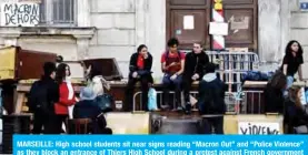  ?? — AFP ?? MARSEILLE: High school students sit near signs reading “Macron Out” and “Police Violence” as they block an entrance of Thiers High School during a protest against French government education reforms yesterday.