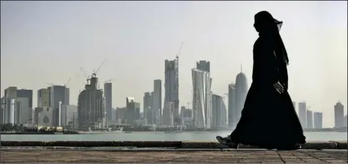  ?? The Associated Press ?? QATAR: In this May 14, 2010, photo, a Qatari woman walks in front of the city skyline in Doha, Qatar. An investigat­ion into why a British man fell to his death on a Qatar World Cup site has raised concerns about stadium roof safety. Acting as a mediator, Kuwait has presented Qatar a long-awaited list of demands from Saudi Arabia, Bahrain, the United Arab Emirates and Egypt, four Arab nations that cut ties with Qatar in early June.