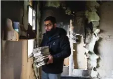  ?? CHRISTOPHE­R KATSAROV/THE CANADIAN PRESS ?? Usama Zahid removes the Qur’an and other books from shelves Sunday, as congregati­on members clean up debris from the deliberate­ly set fire.