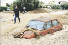  ?? AP PHOTO/PETROS GIANNAKOUR­IS ?? A man walks next to a damaged car after floods in the town of Agria near the city of Volos, Greece, on Thursday.
